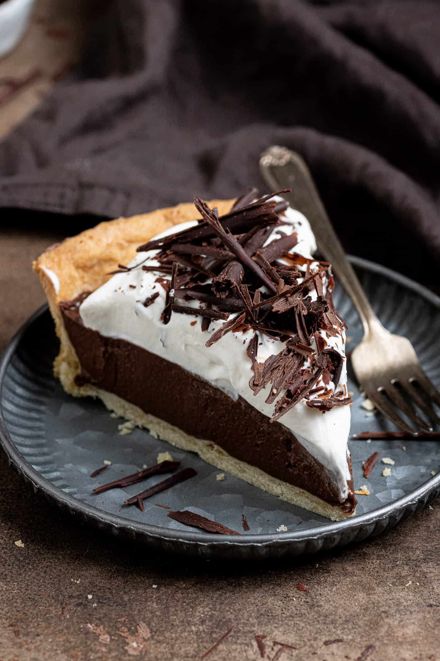 A slice of vegan chocolate cream pie on a metal plate with a fork.