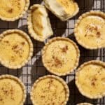 Flatlay of vegan custard tarts on a wire cooling rack, one broken in half.