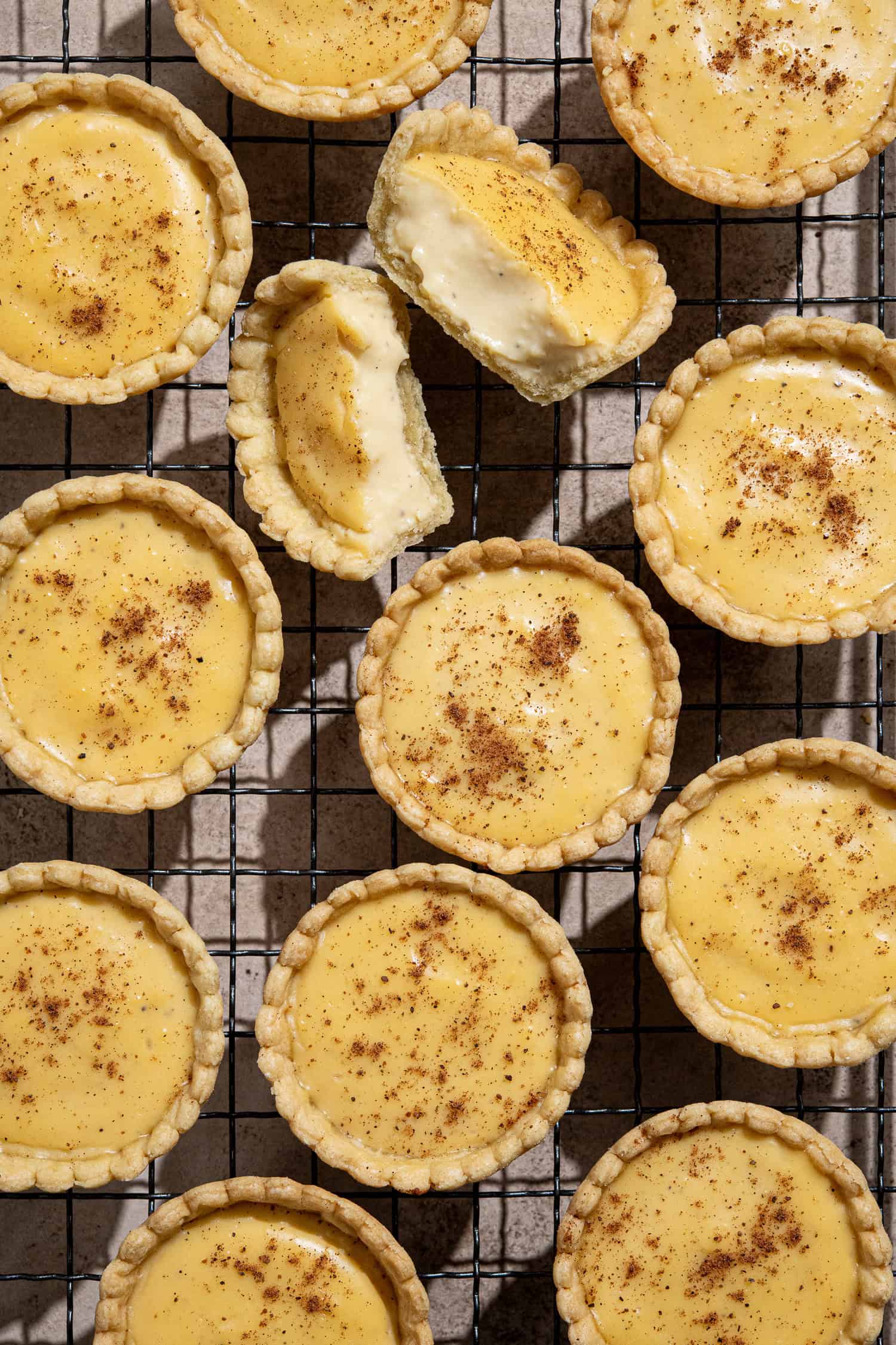 Flatlay of vegan custard tarts on a wire cooling rack, one broken in half.