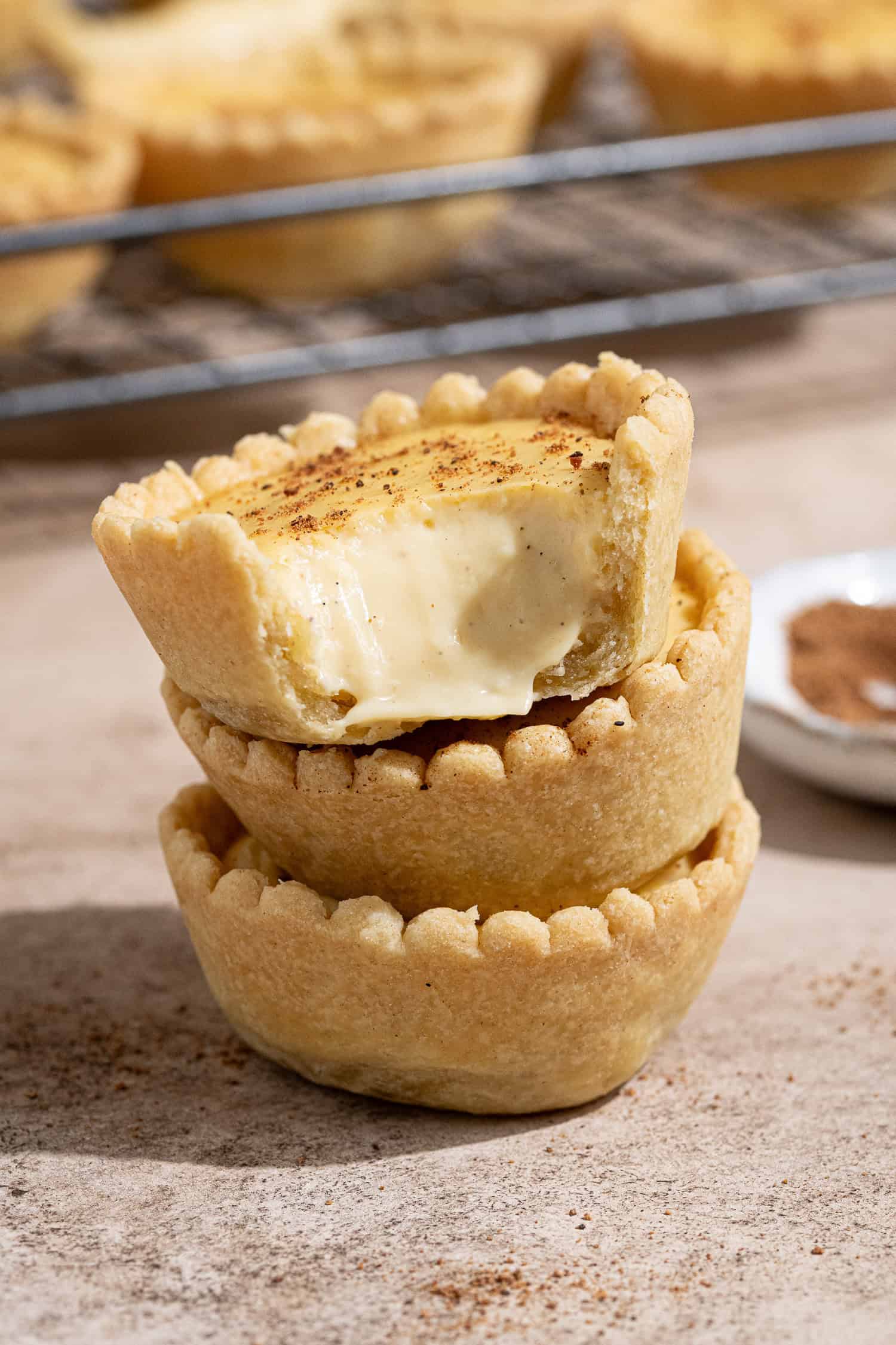 A stack of three vegan custard tarts, the top one with a bite taken out of it.