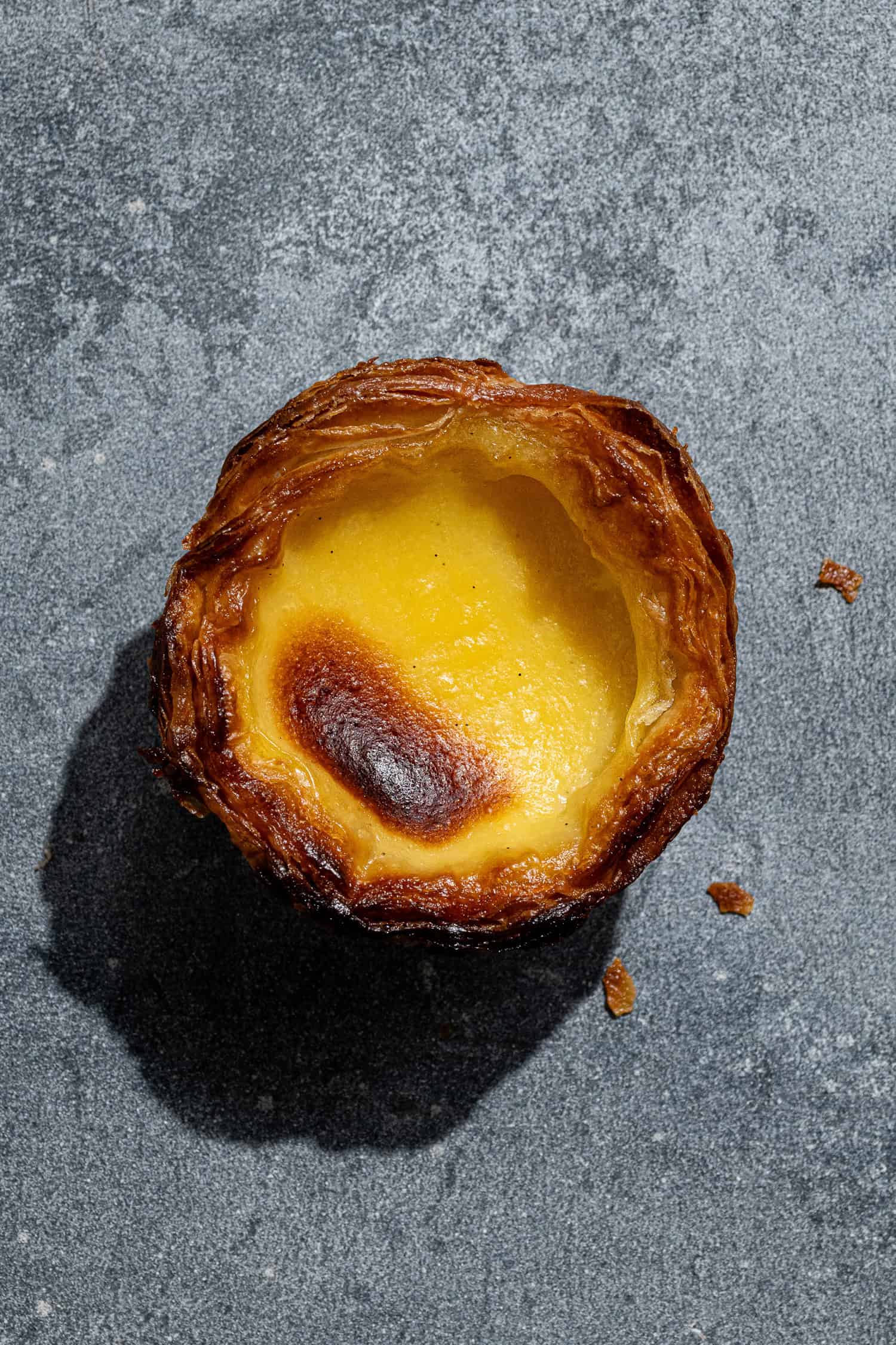 A vegan pasteis de nata on a grey surface.