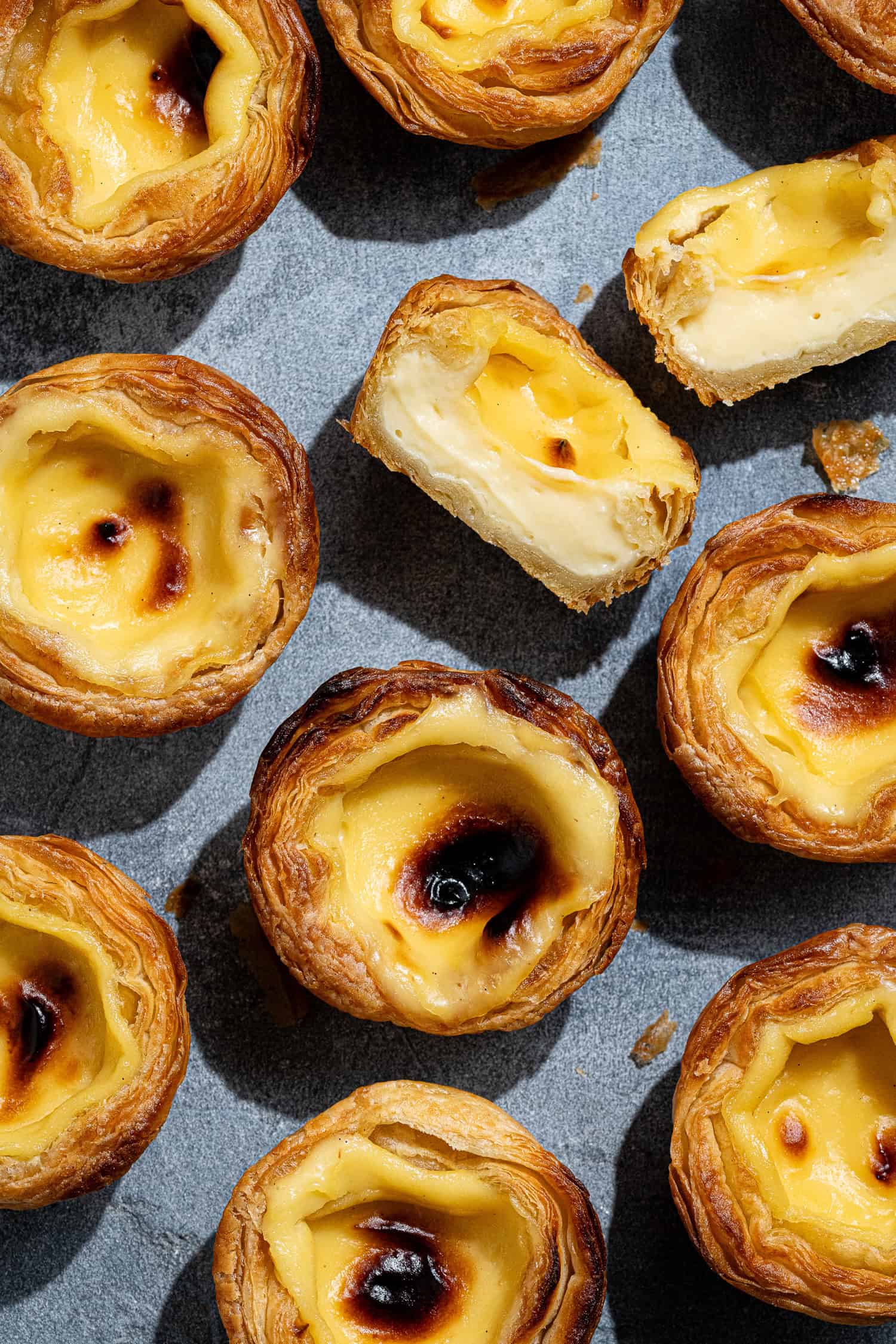 Flatlay of vega pasteis de nata on a grey surface, one sliced in half.