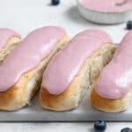 A row of vegan iced buns on a marble board with a bowl of pink icing.