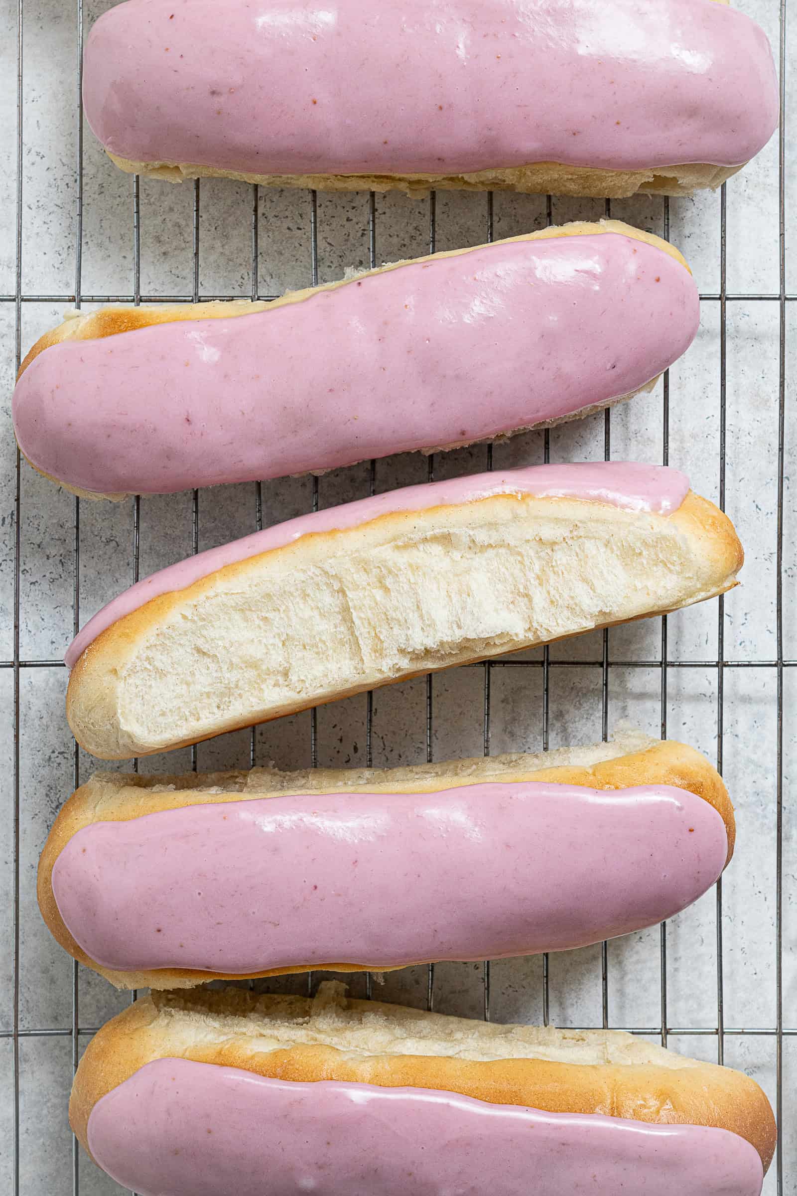 A row of vegan iced buns on a wire cooling rack, one on it's side.