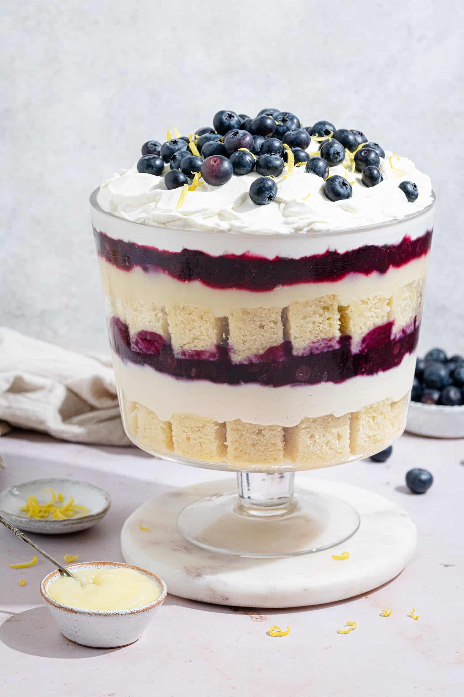 Vegan lemon blueberry trifle in a glass trifle bowl on a marble board.