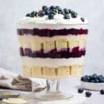 Vegan lemon blueberry trifle in a glass trifle dish with bowls of blueberries and lemon curd.