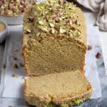 Vegan pistachio loaf cake on a marble board with a slice cut, a bowl of pistachios in the background.