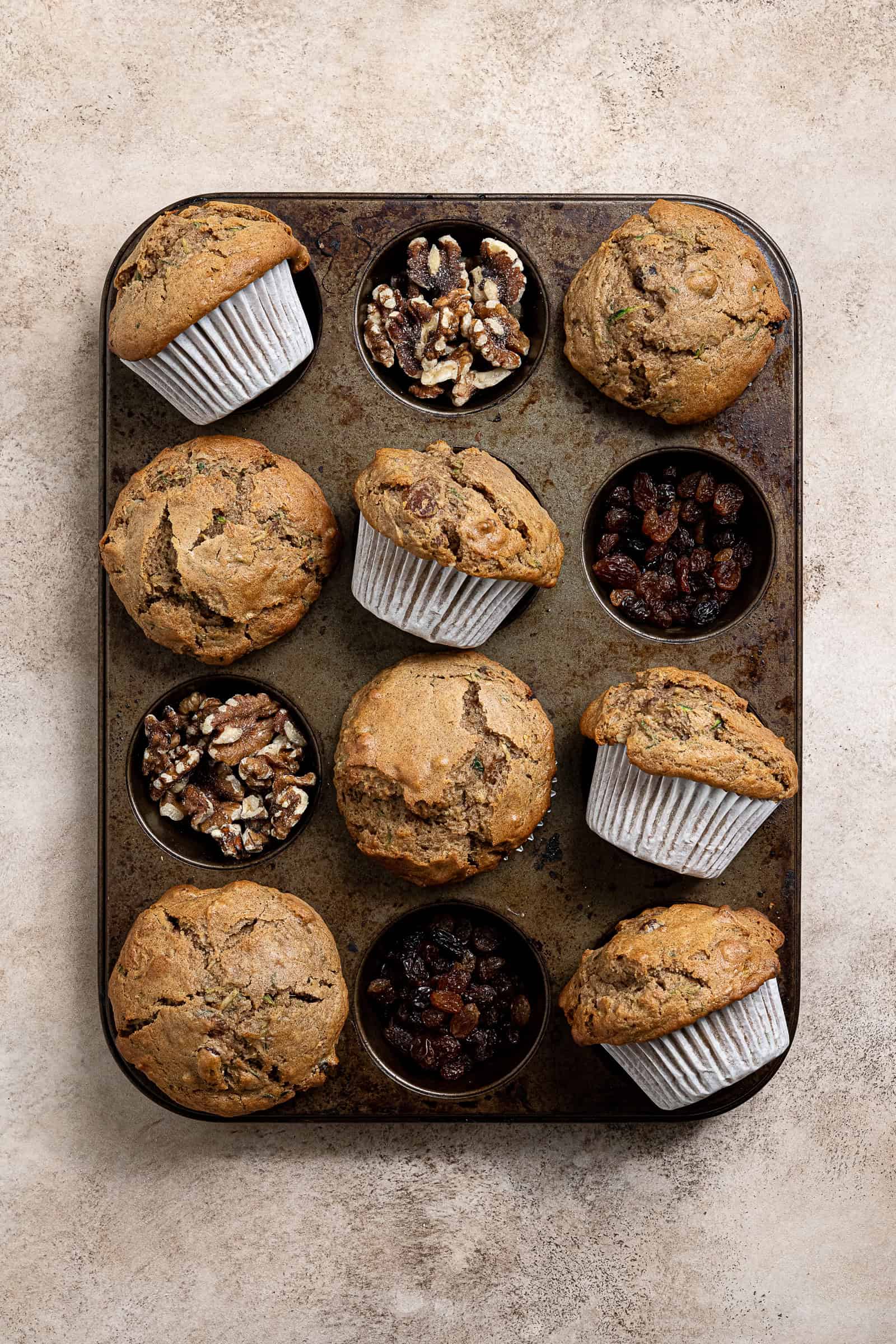 Vegan courgette muffins in a muffin tray, with the empty cavities filled with sultanas and walnuts.