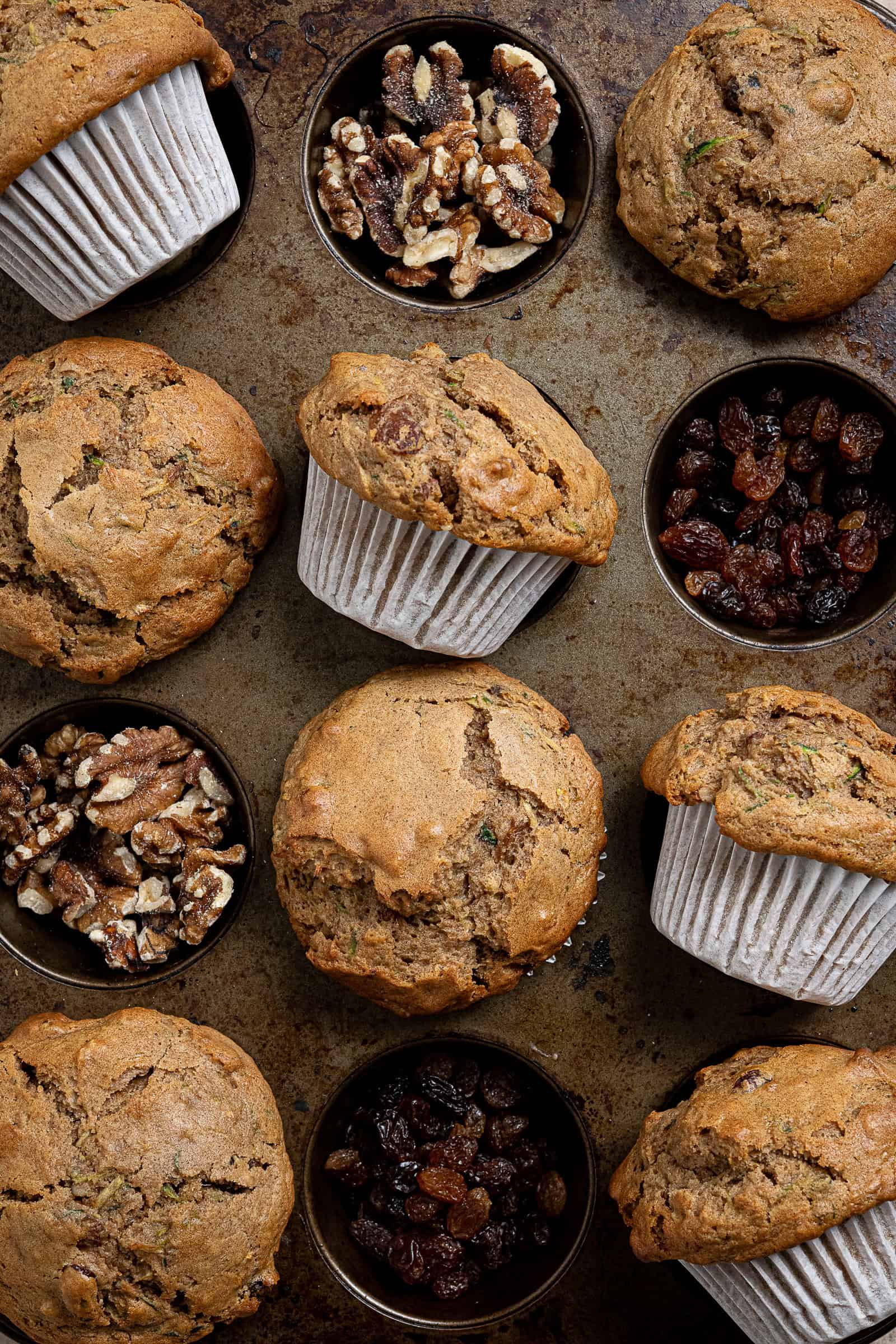 Close up shot of vegan courgette muffins in a muffin tin with sultanas and walnuts filling the empty cavities.