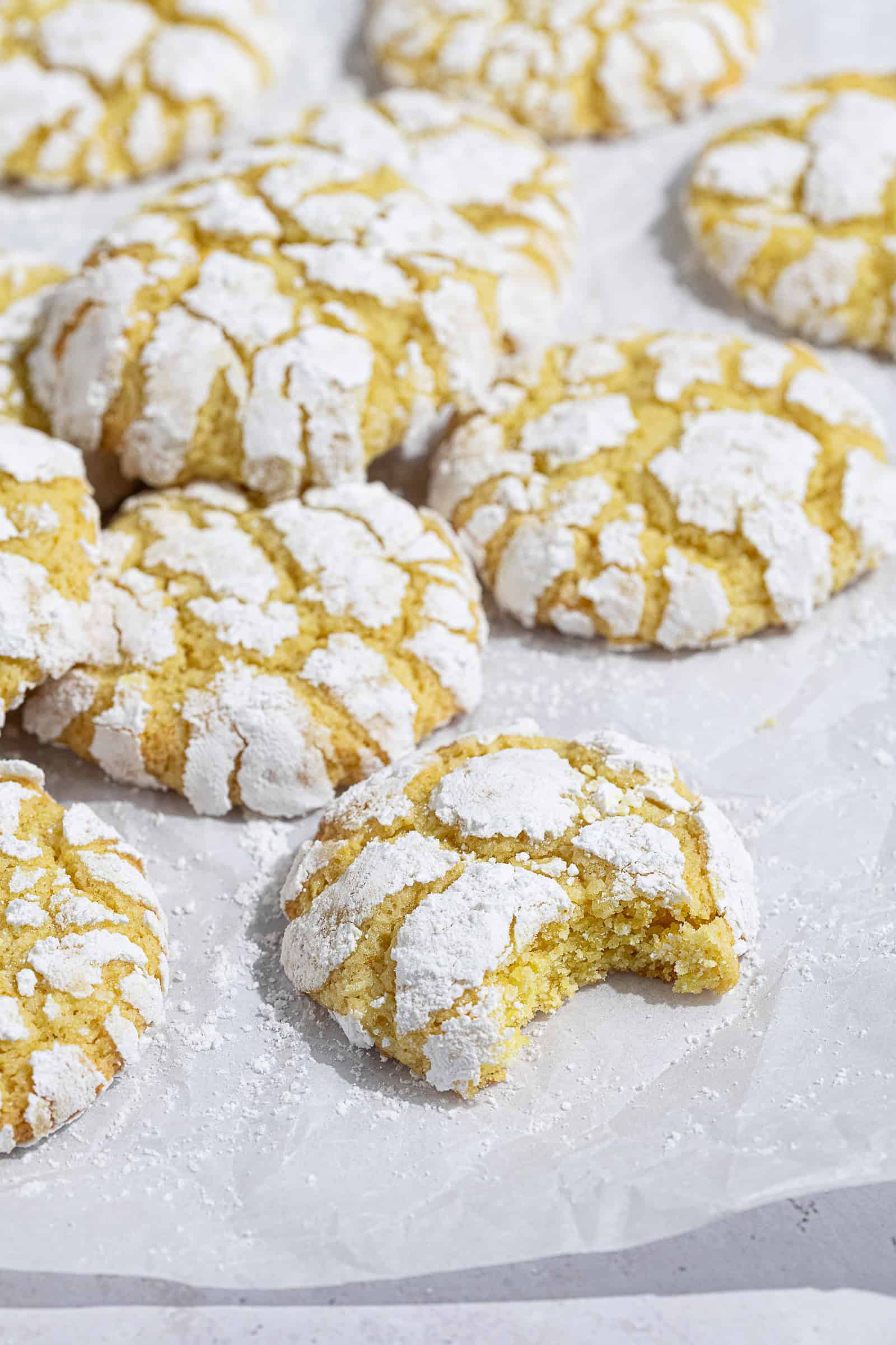 Vegan lemon crinkle cookies on a sheet of baking paper, one with a bite taken out of it.