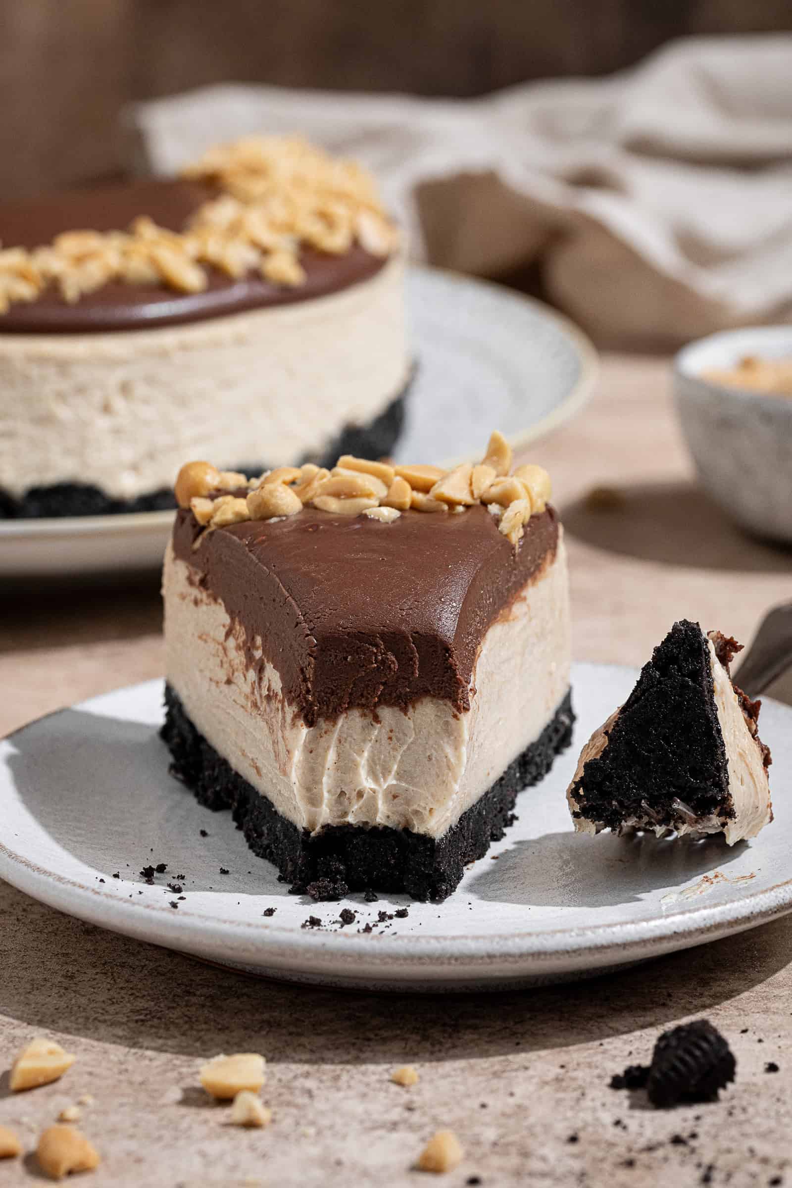 Close up shot of a slice of peanut butter cheesecake on a white plate with a forkful taken out of it.