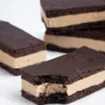 Close up shot of vegan coffee ice cream sandwiches on a sheet of baking paper, one with a bite taken out of it.