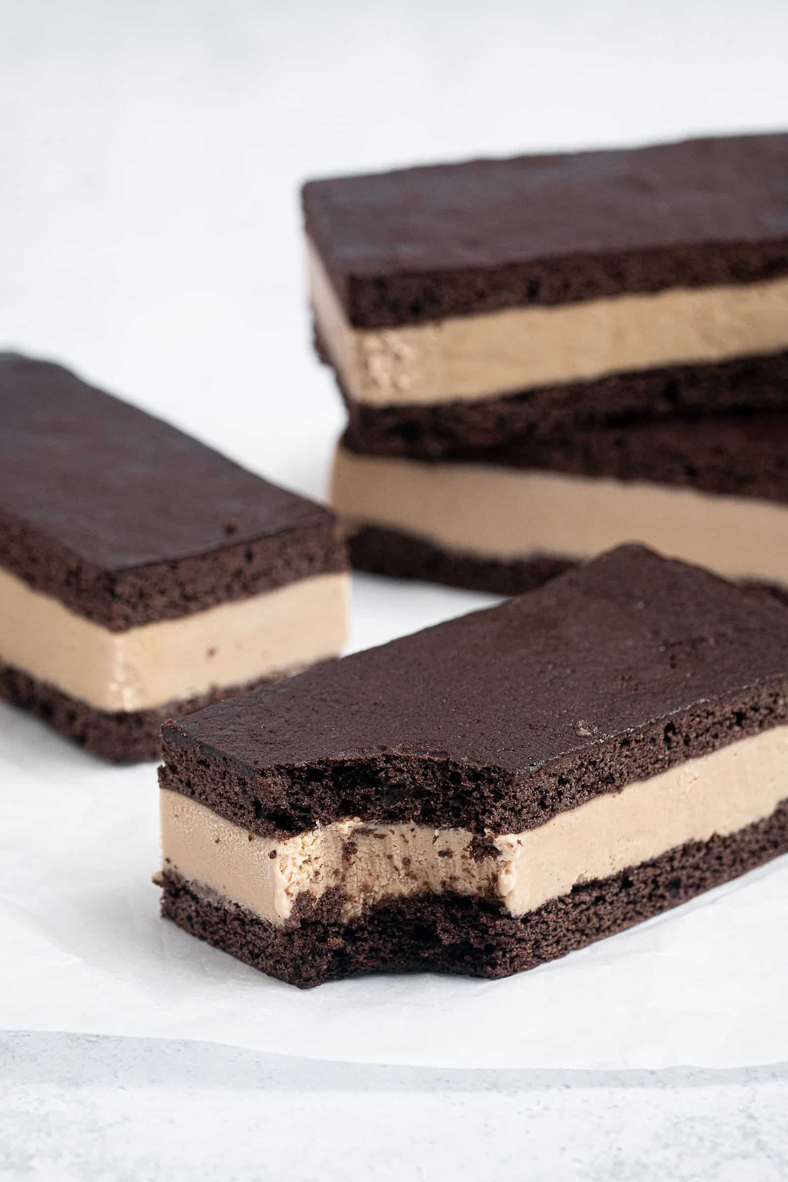 Close up shot of vegan coffee ice cream sandwiches on a sheet of baking paper, one with a bite taken out of it.