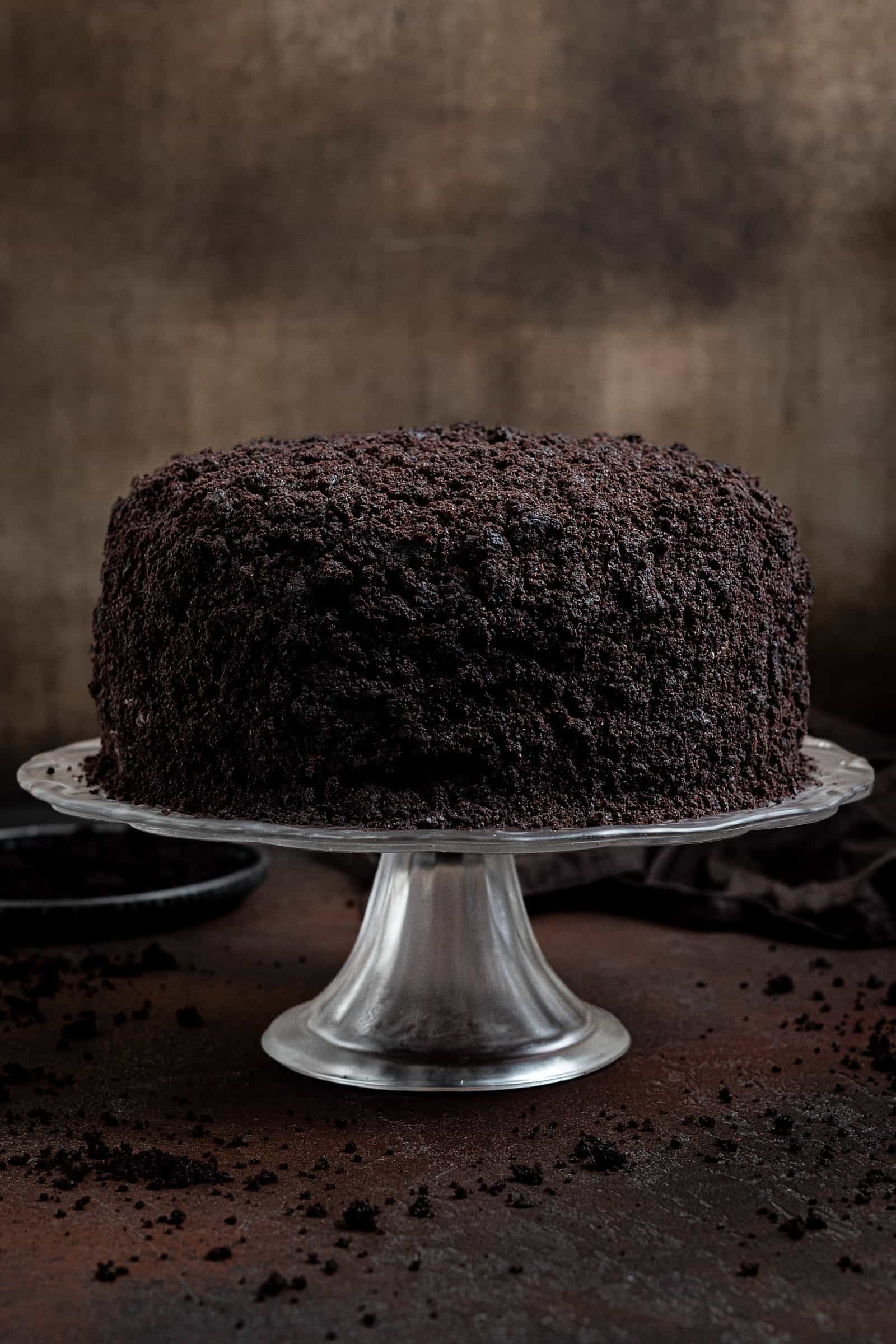 Vegan Brooklyn blackout cake on a glass cake stand on a dark background.