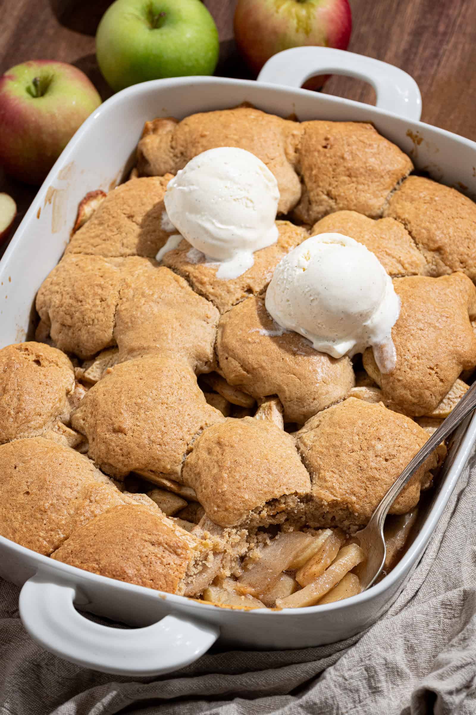 Vegan apple cobbler in a white baking dish with two scoops of ice cream on top.