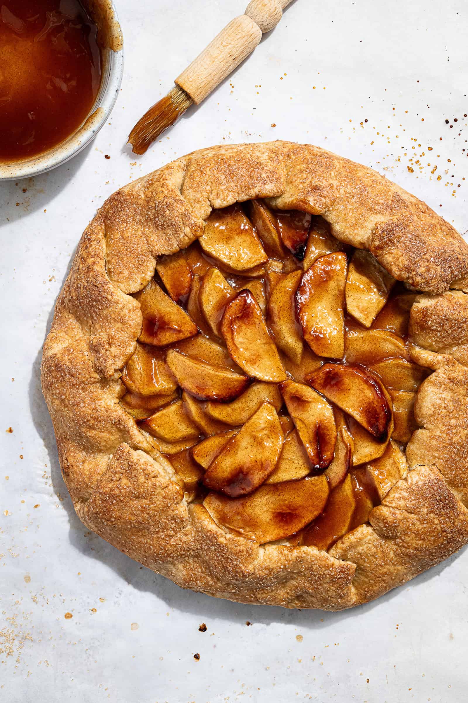 Flatlay of the vegan apple galette with a bowl of glaze and a pastry brush.
