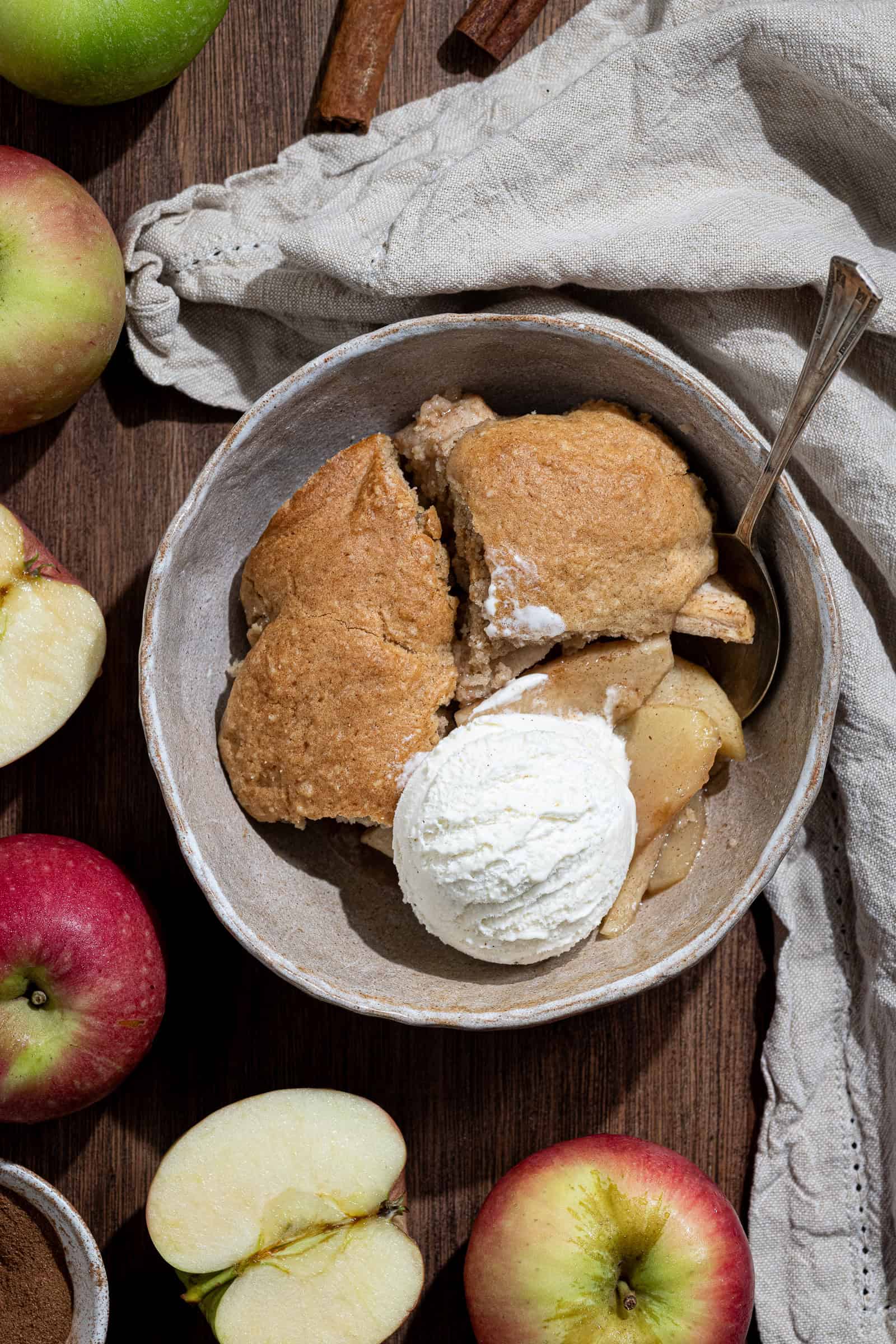 A portion of vegan apple cobbler in a bowl with a scoop of ice cream.