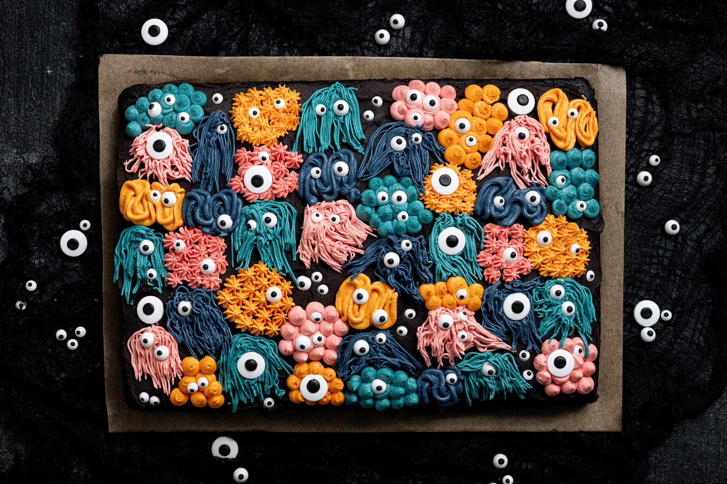 Halloween monster decorated black velvet sheet cake on a black surface surrounded by candy eyes.