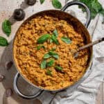 Creamy marry me orzo in a pan on a tiled surface with a bunch of fresh basil and salt and pepper shakers.