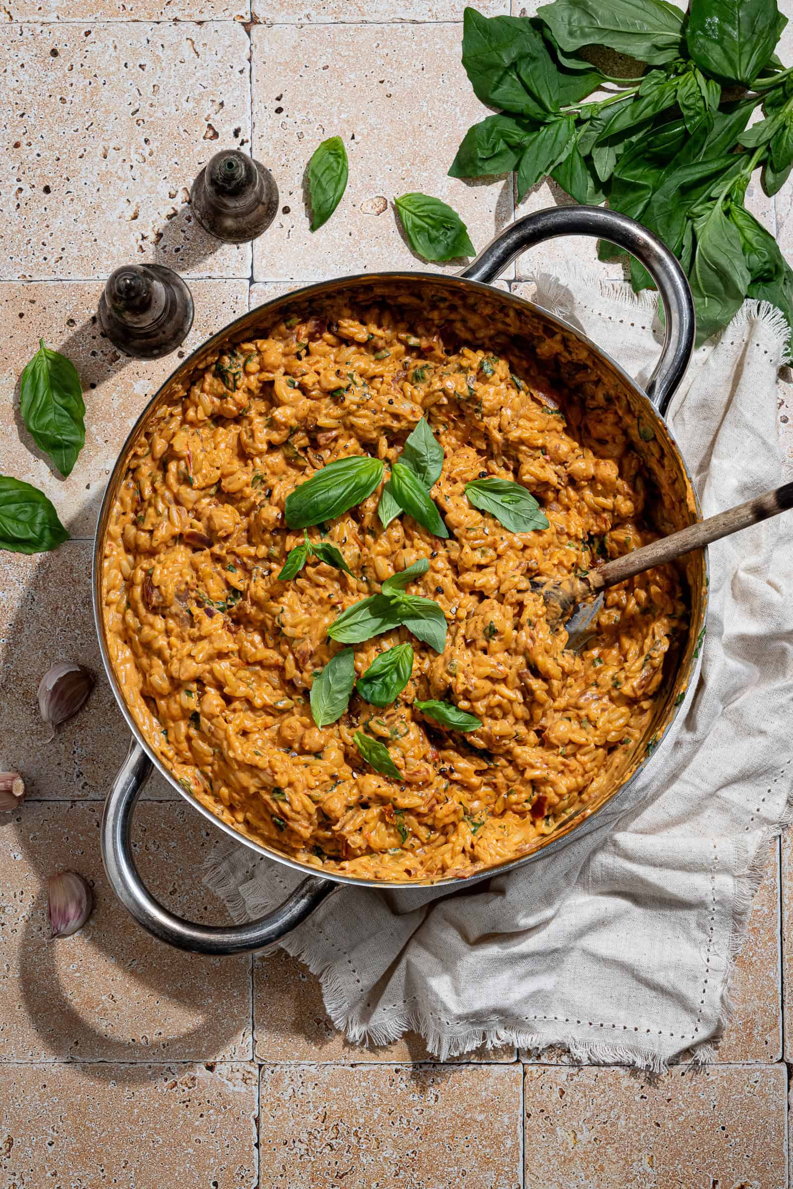 Creamy marry me orzo in a pan on a tiled surface with a bunch of fresh basil and salt and pepper shakers.