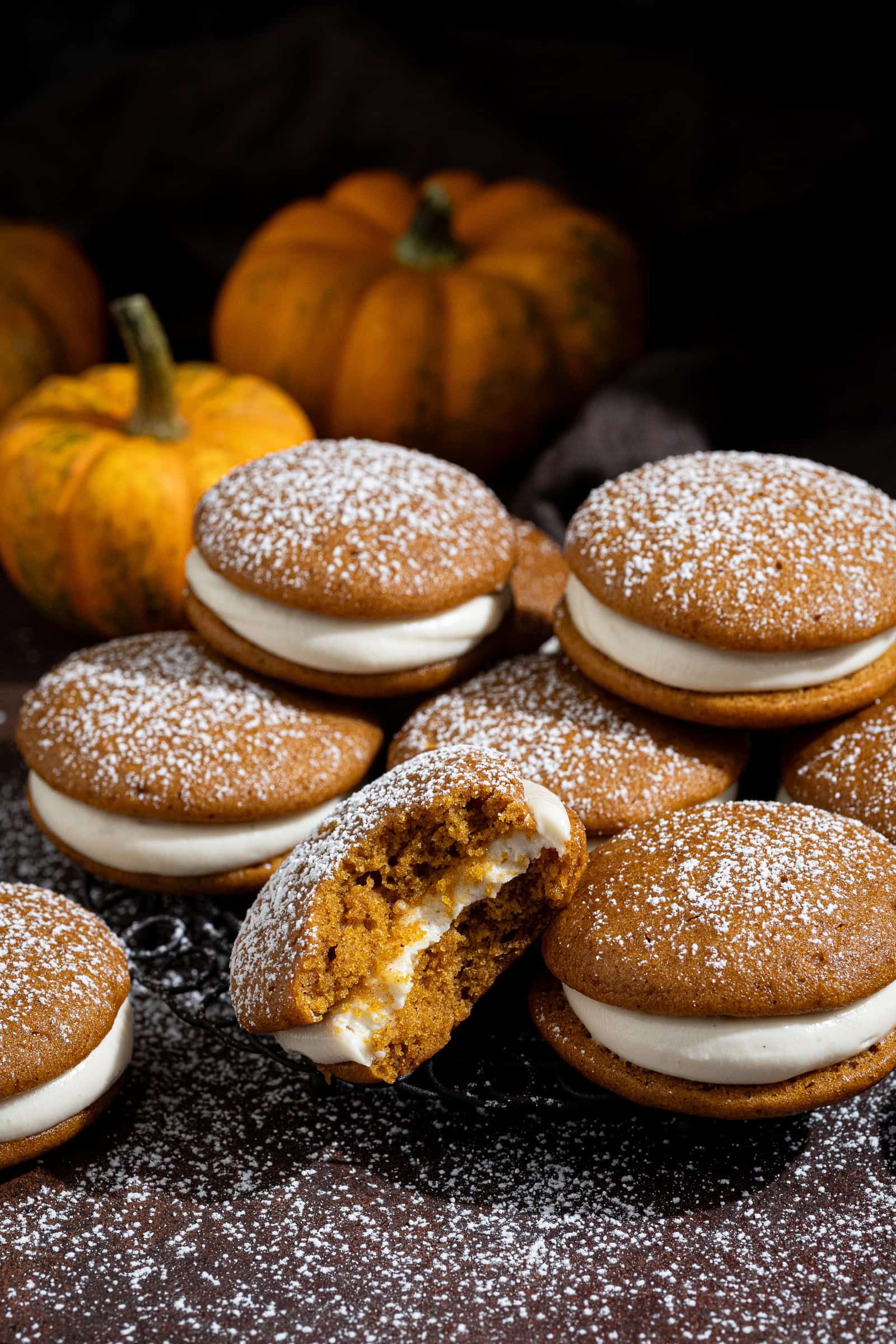 Vegan pumpkin whoopie pies stacked on a wire plate, with mini pumpkins in the background.