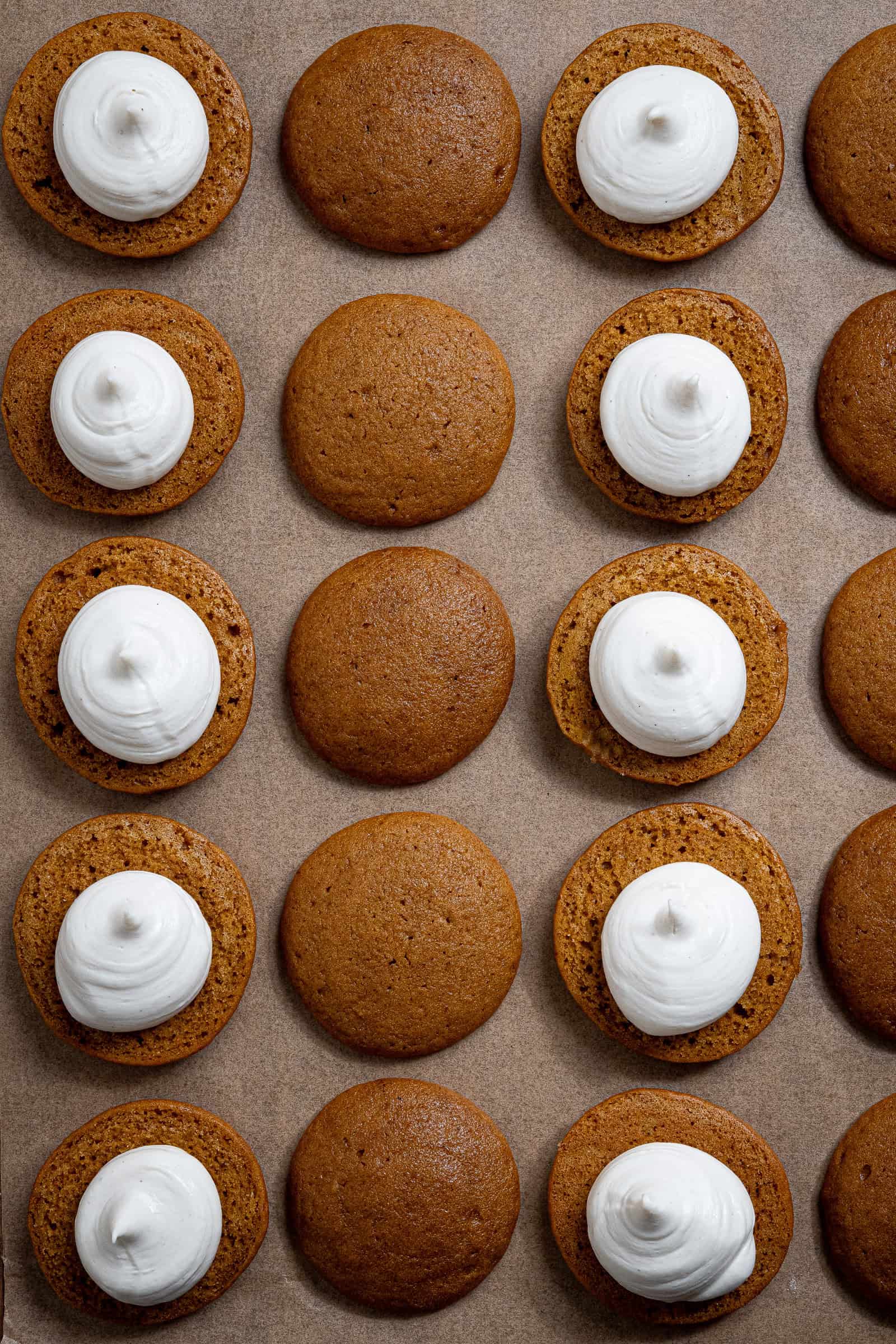 Rows of cookies for whoopie pies with cheesecake filling piped onto half of them.