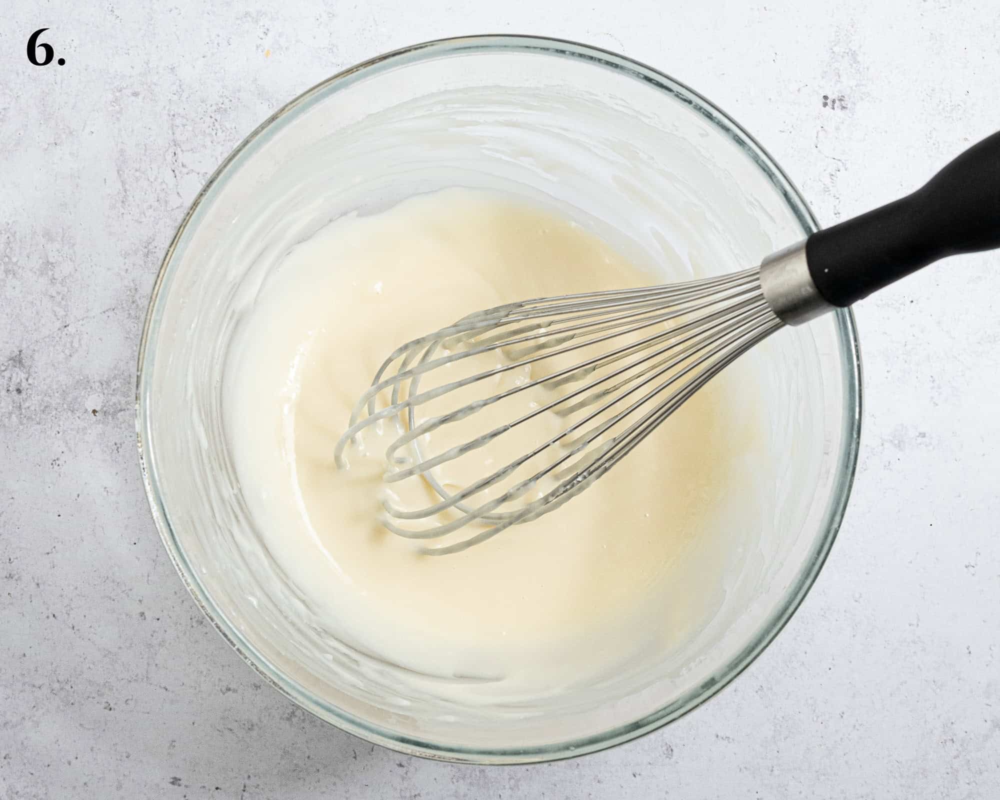 Step 6, the white chocolate cream cheese glaze in a bowl with a whisk.