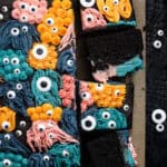Vegan black velvet sheet cake with buttercream monster decorations with four slices cut.