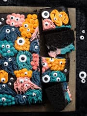 Vegan black velvet sheet cake with buttercream monster decorations with four slices cut.