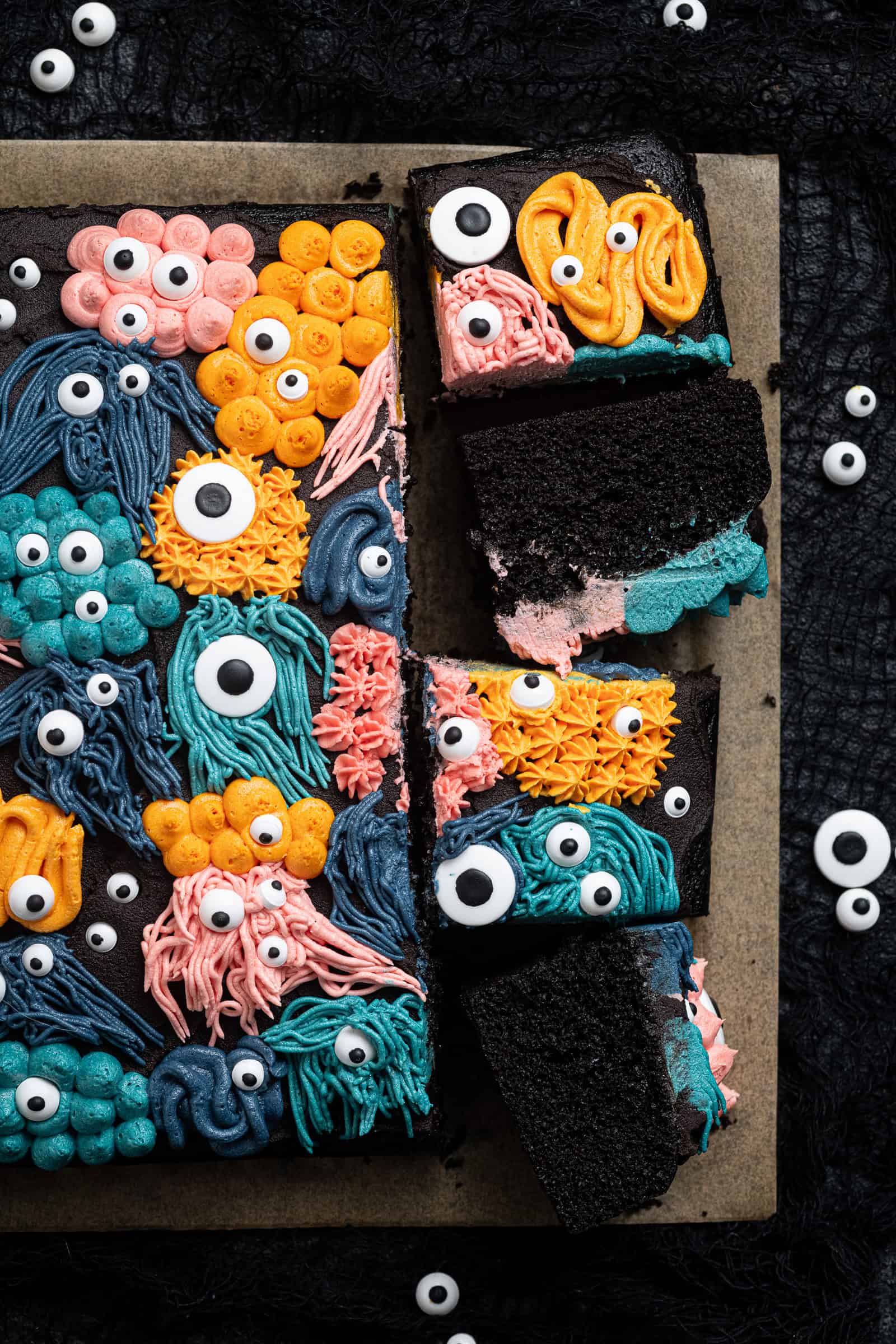 Vegan black velvet sheet cake with buttercream monster decorations with four slices cut.