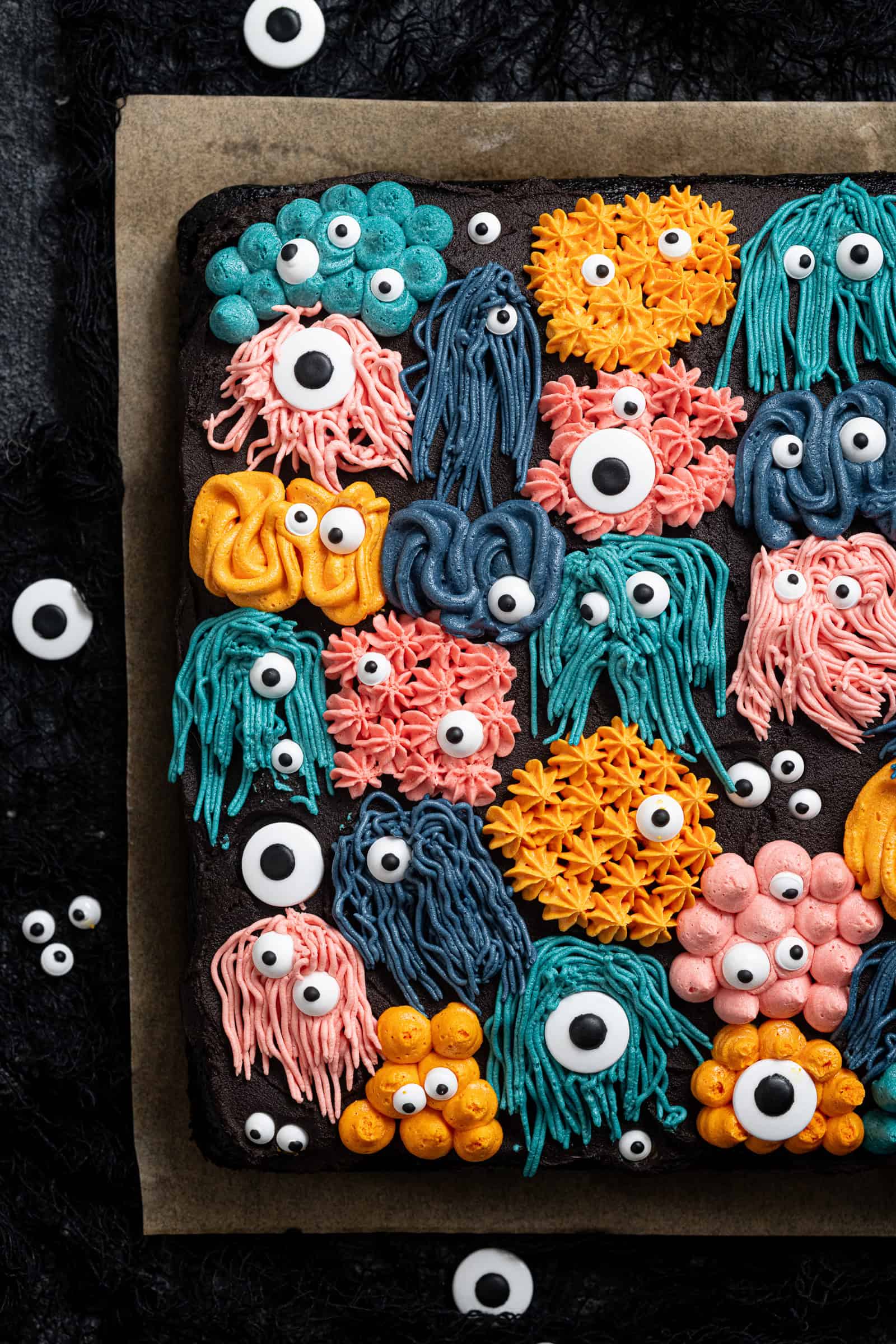 Vegan black velvet sheet cake on a sheet of baking paper surrounded by candy eyes.