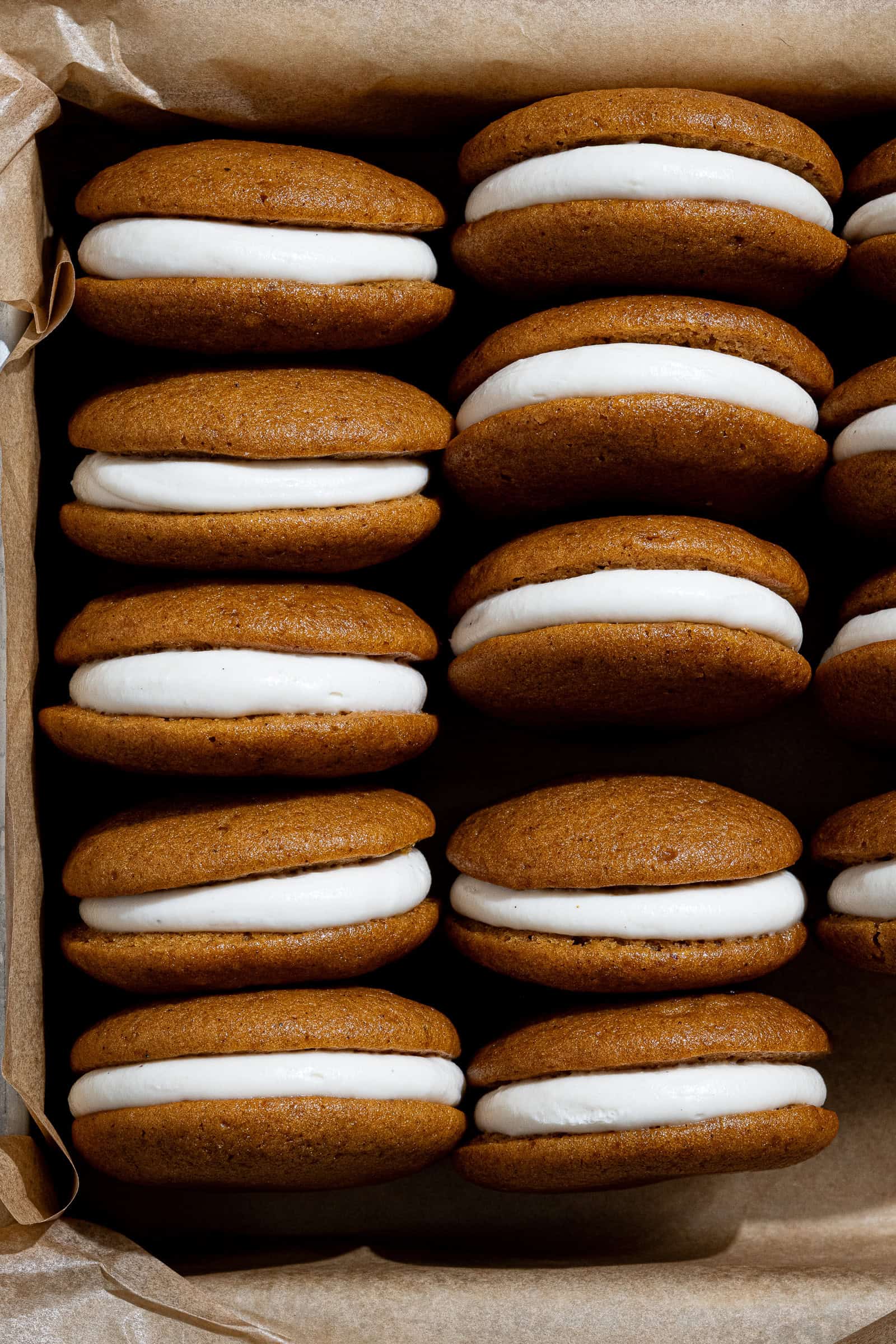 Rows of vegan pumpkin whoopie pies in a parchment lined tin.