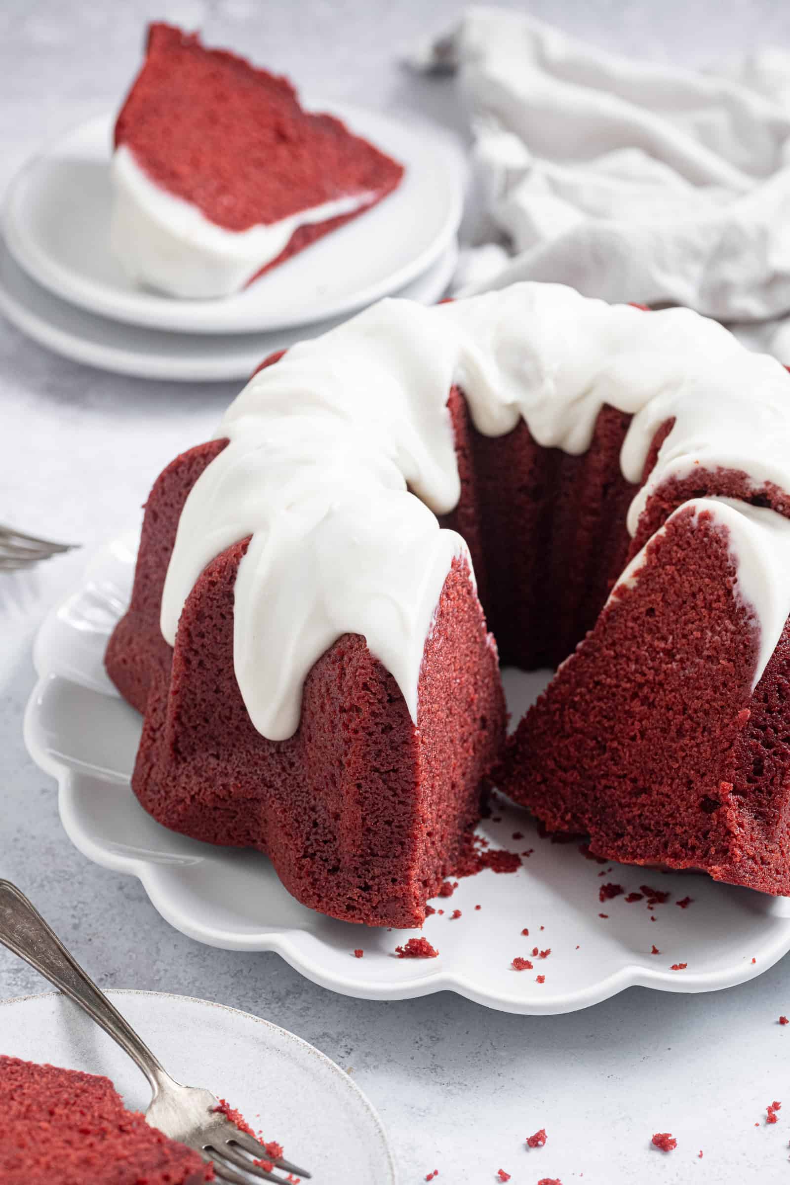 Vegan red velvet bundt cake on a white plate with a couple of slices cut out.